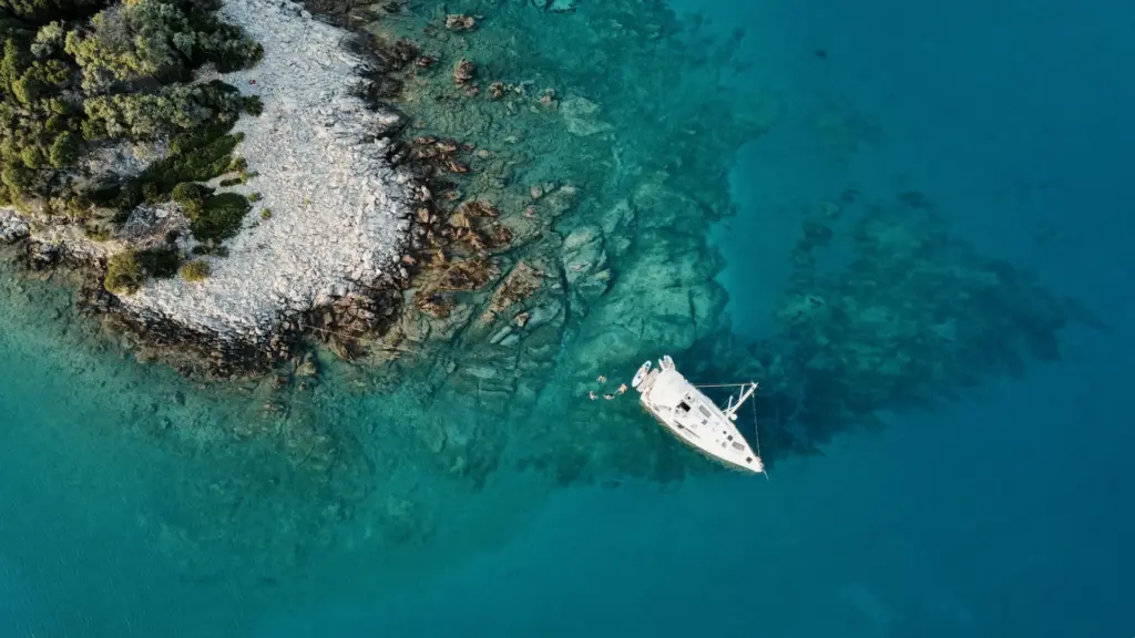 Segelboot liegt an einer krooatischen Küste mit türkisblauem Meer und Menschen baden im Meer