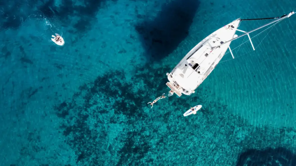 Vogelperspektive von einem Segelboot dass auf einem türkisblauem Meer schwimmt und Menschen baden im Wasser