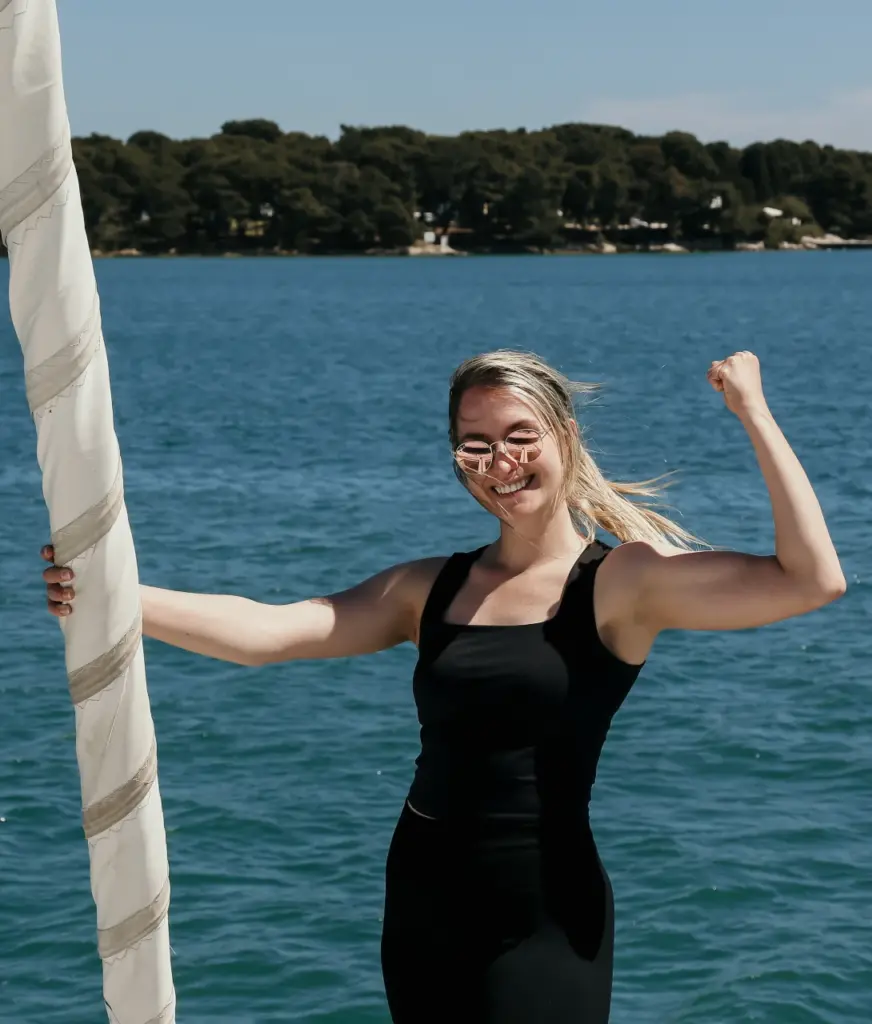 Manuela Nikolic ist schwarz gekleidet und steht am Segelboot. Sie lächelt in die Kamera und ballt die Faust