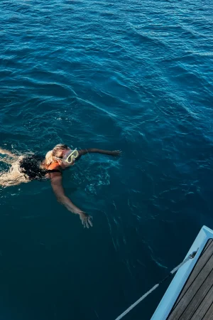 Frau mit schwarzem Badeanzug und Taucherbirlle schwimmt im Meer Richtung Boot